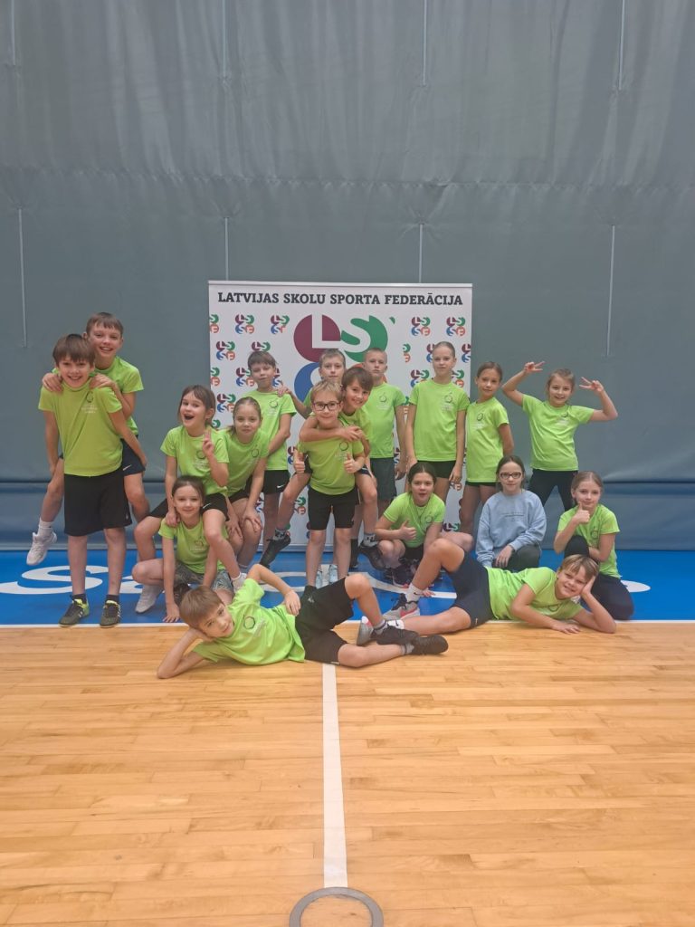 Skolēni zaļos t-kreklos pozē sporta zālē